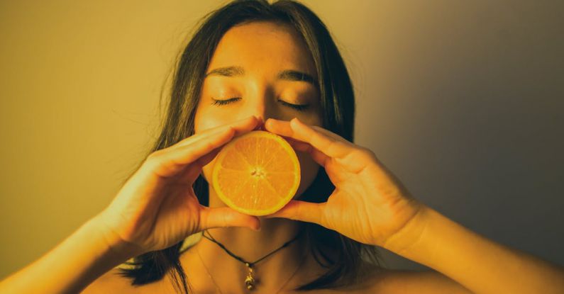 Immune Boost - Attractive woman with eyes closed holding orange slice against lips