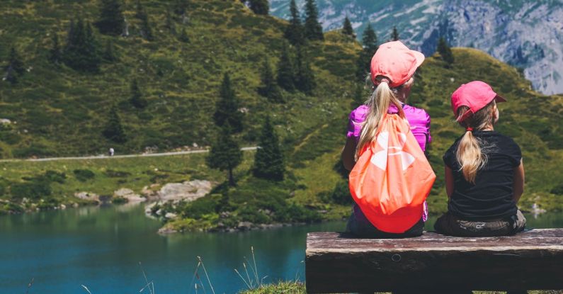 Travel Kids - Two Girls Sitting on Brown Bench Near Body of Water