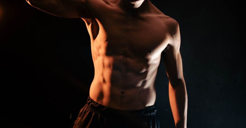 Regular Exercise - A shirtless man flexing his muscles in the dark