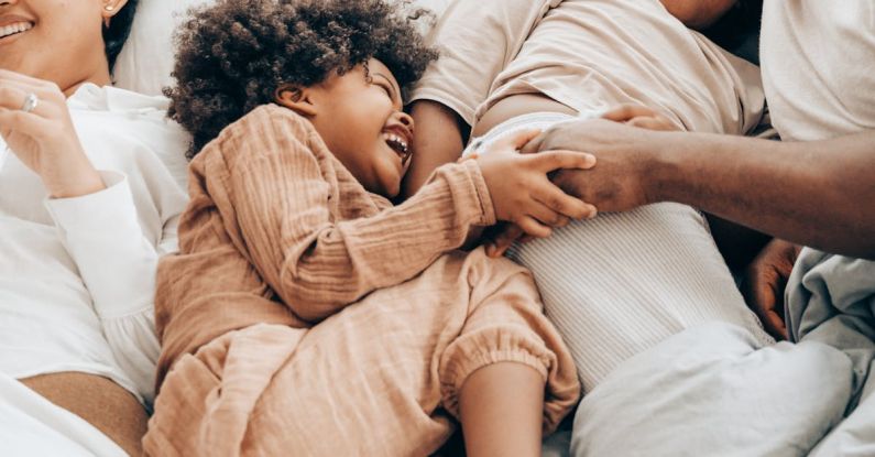 Sibling Bonding - From above of smiling ethnic kids playing with father while resting together on bed lying near mother
