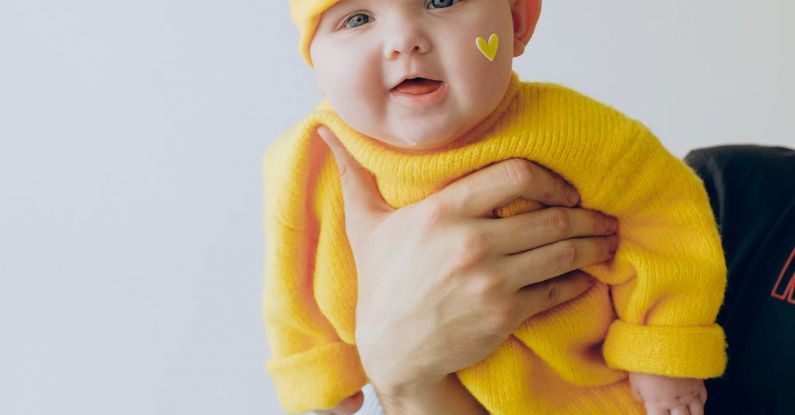 Co-parenting - Crop parent holding smiling baby in arms against gray wall in room