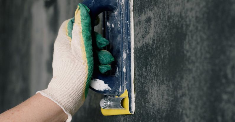 Home Tools - Crop anonymous male worker in gloves holding scraper and aligning walls in flat